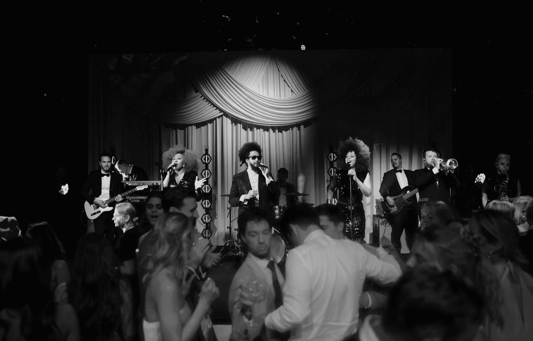 Black and white photo of a live musical band performing on stage while guests dance
