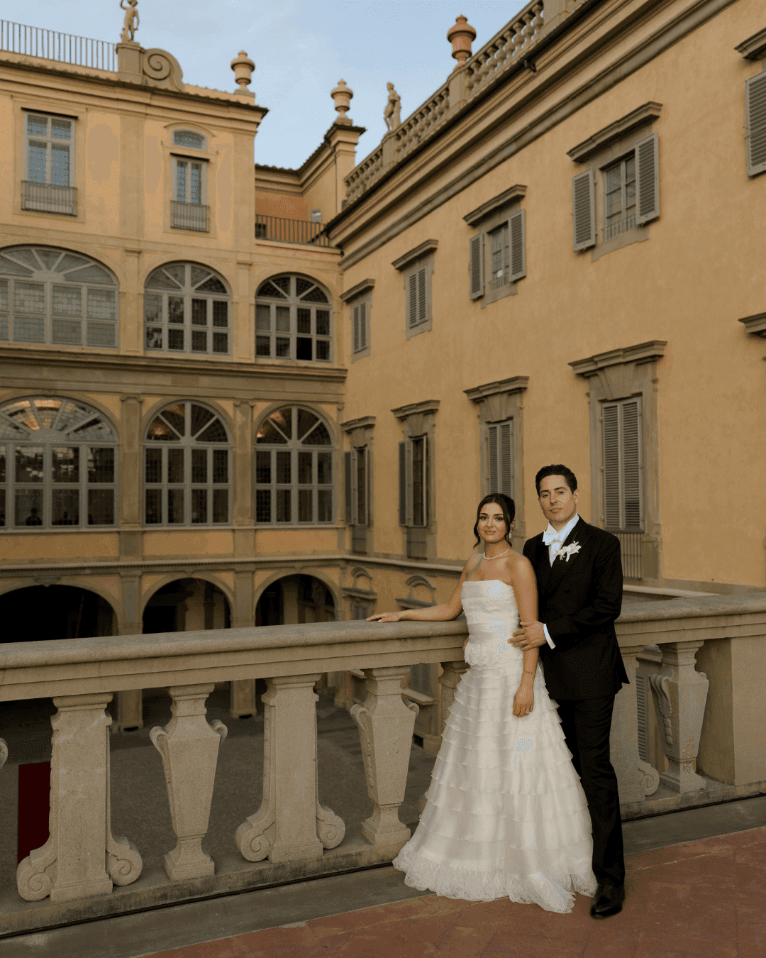 Bride and groom posing on the stone balcony of a classical Italian palazzo courtyard